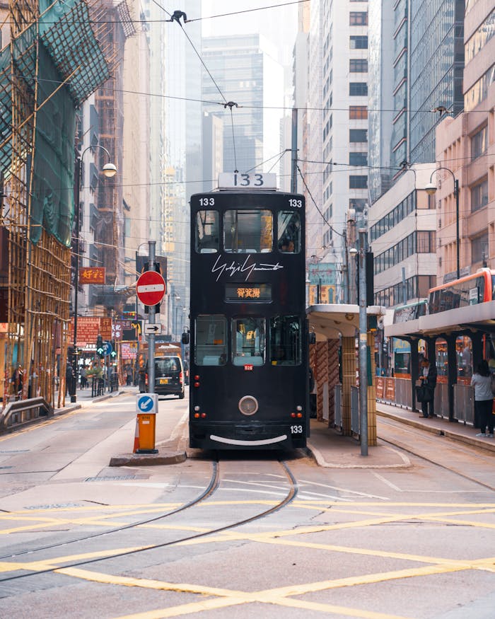 Classic black tram navigating Hong Kong's dynamic city streets under daylight.